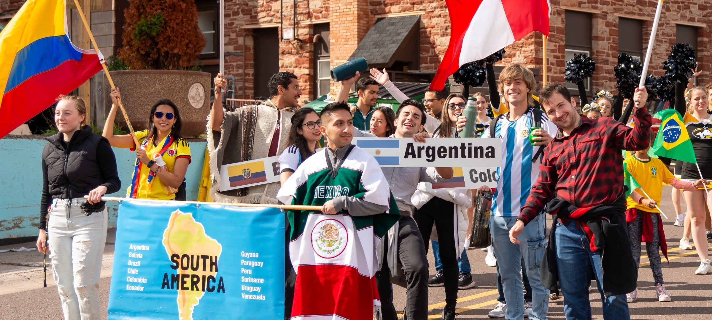 Student walking in Parade of National holding banners that state South America, Argentina, Colombia, and Ecuador