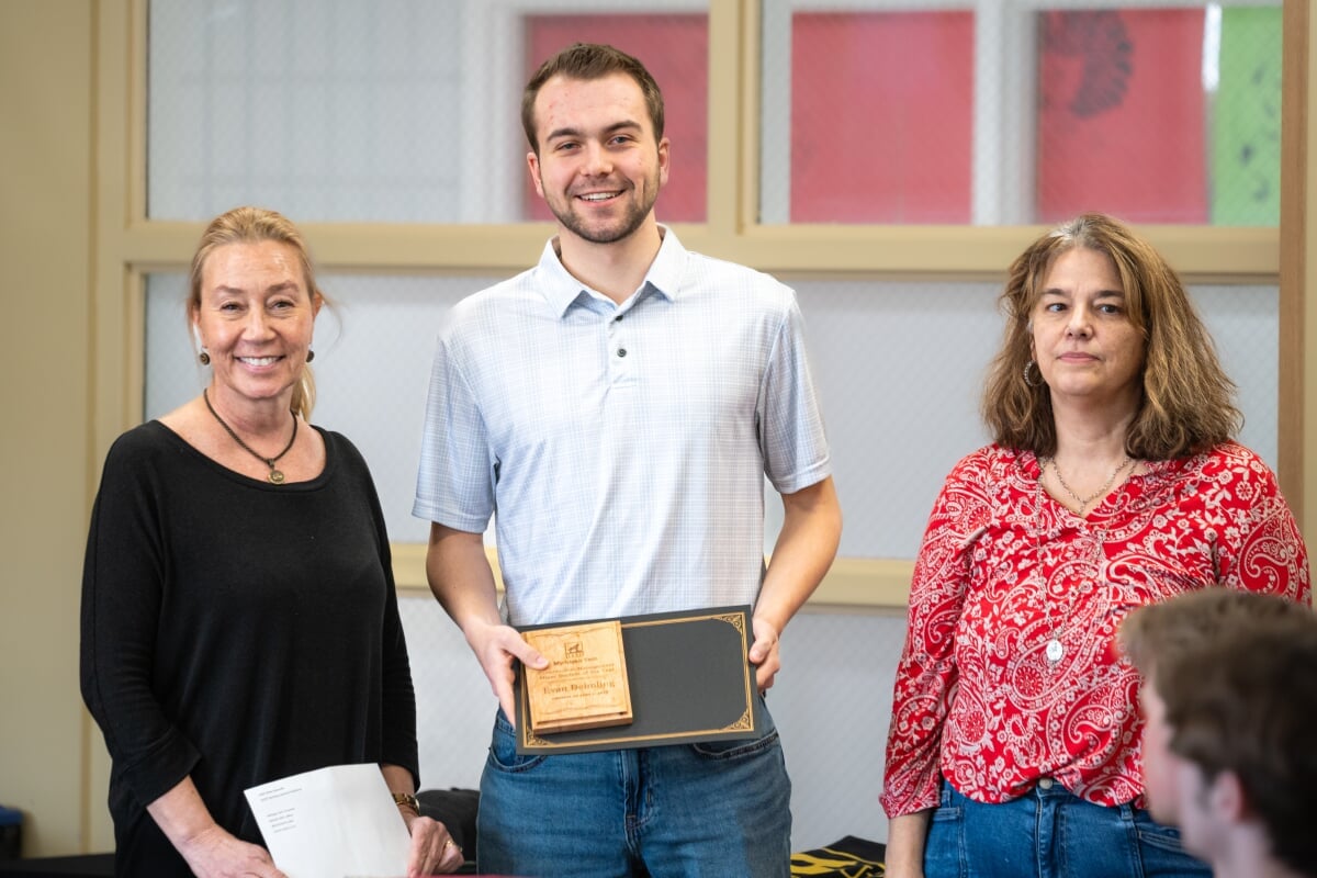 A student holding their award with two faculty members. From left to right - Kerri Sleeman, Evan Deimling, Jen Miller