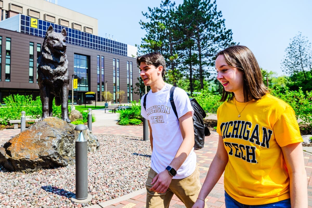 Two students walking in front of the Husky Statue.