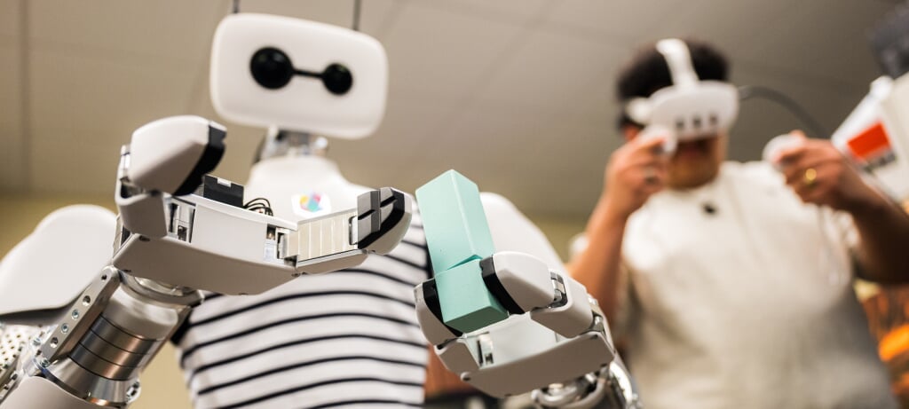 Student using a VR headset and handheld controllers to control Reachy the Robot