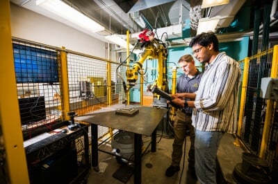 one student and one faculty member working with a robotic arm in a workshop