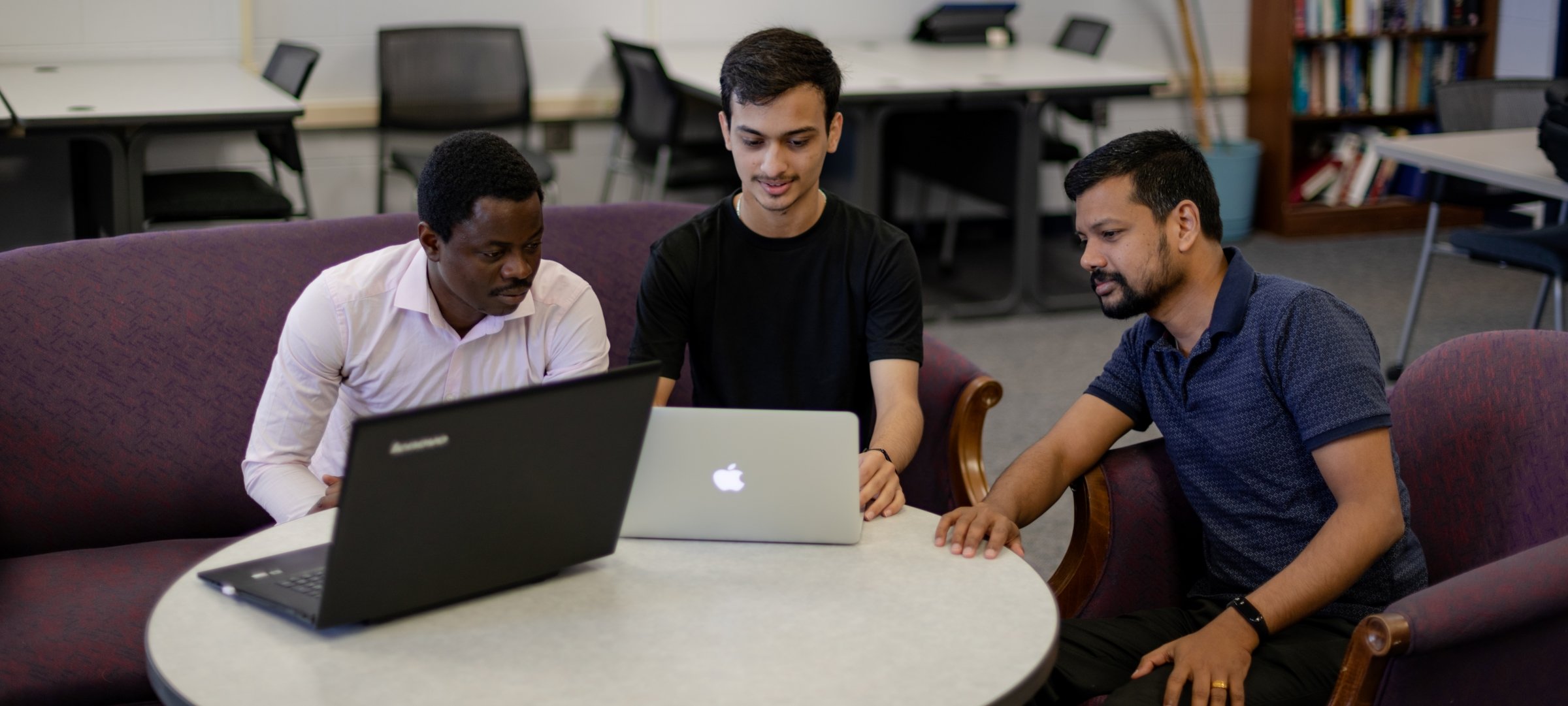 Three grad students sitting in a circle with laptops on a table.