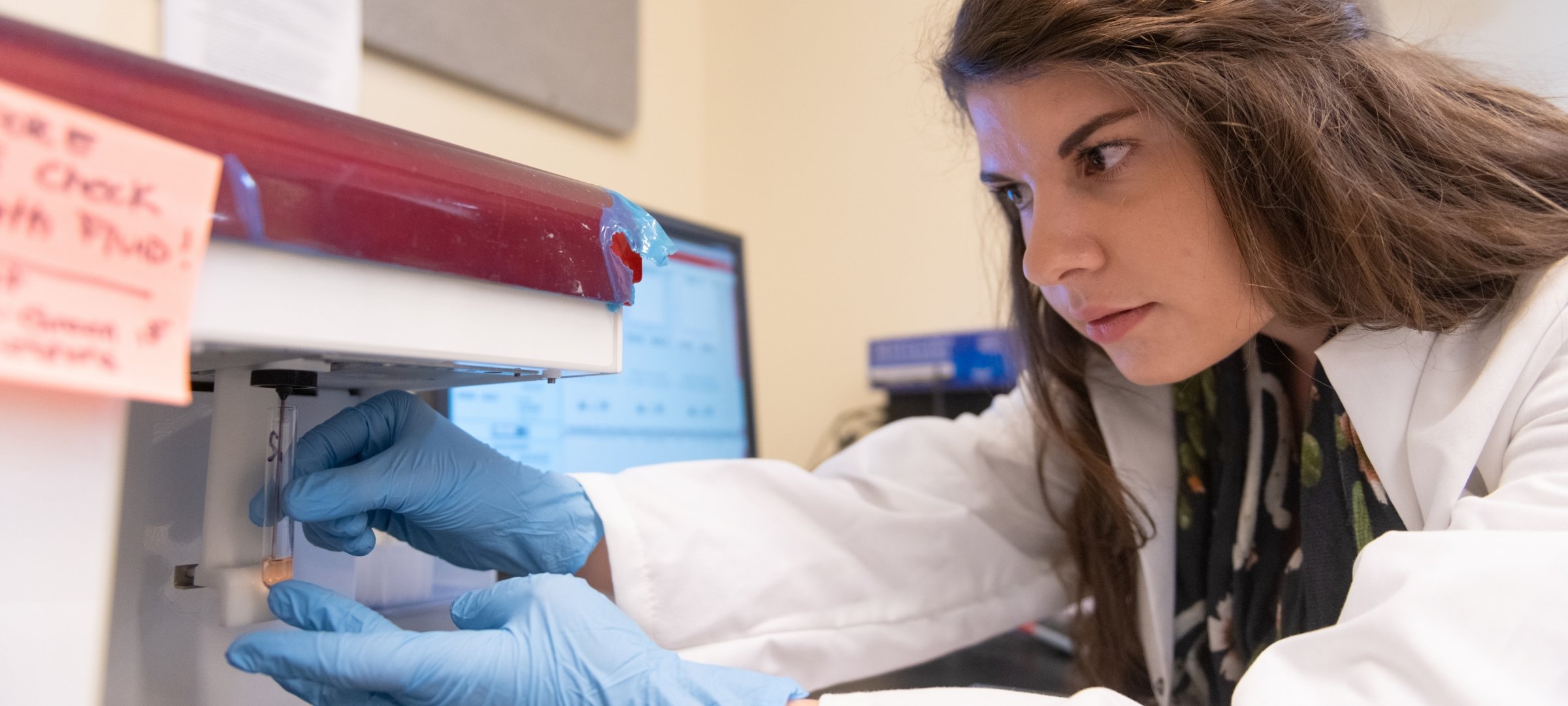 Graduate student inserting a vile into research equipment for analysis.