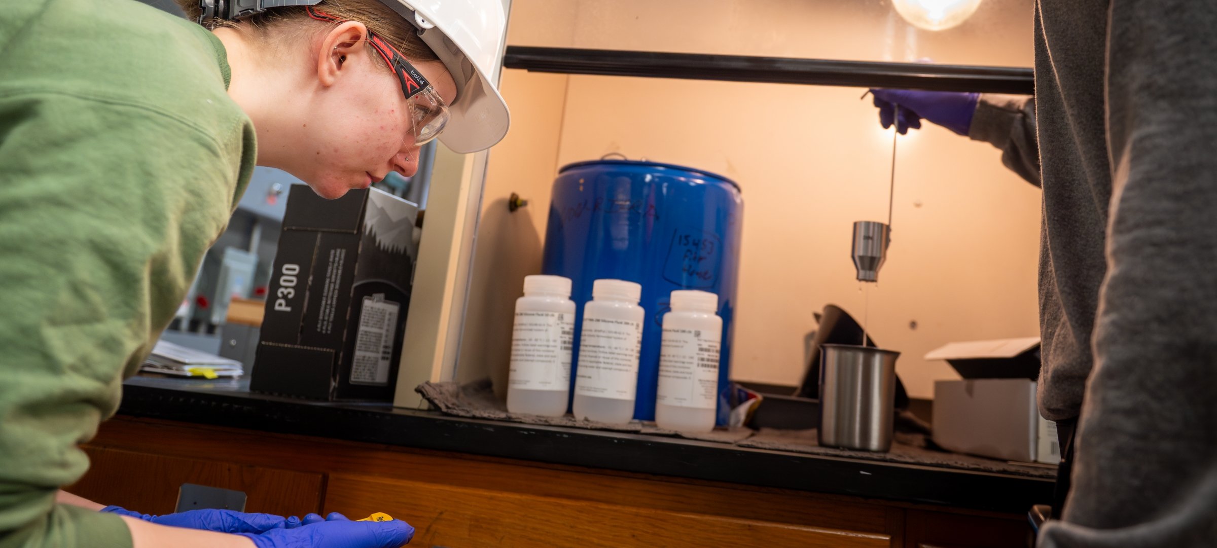 Chemical engineering student working in a lab with safety glasses and hard hat.