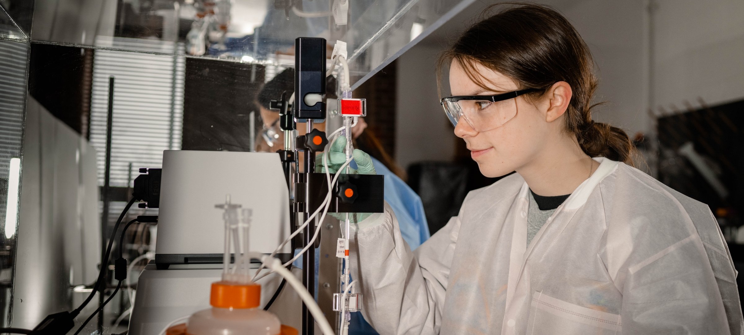 Chemical engineering student working in a lab with lab coat and safety glasses.