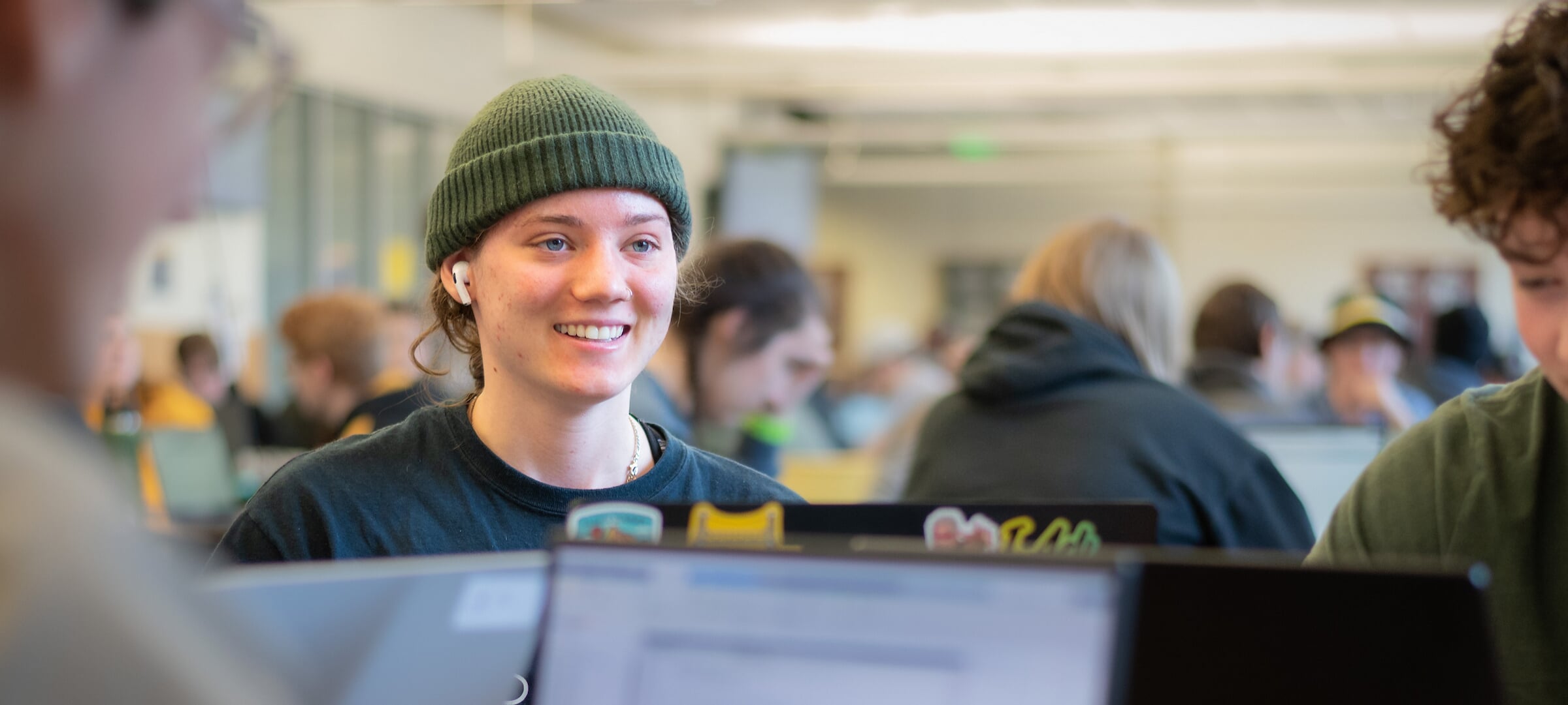 Smiling student working on a laptop with her peers