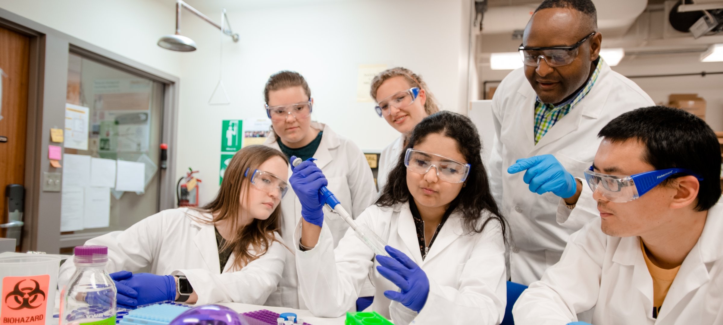 Professor showing students how to take a sample in a lab.