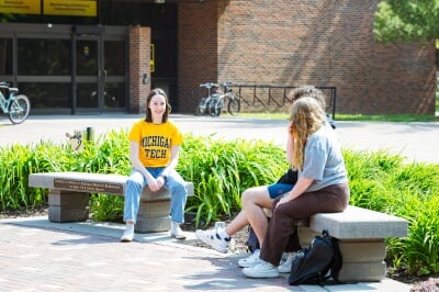 Three students sitting on benches conversing