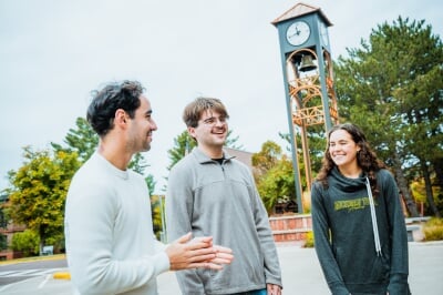 Three students walking and laughing in front of the Michigan Tech bell tower.