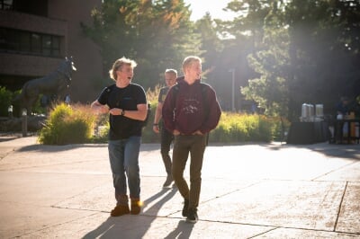 Three students with backpacks walking down a sidewalk and laughing.