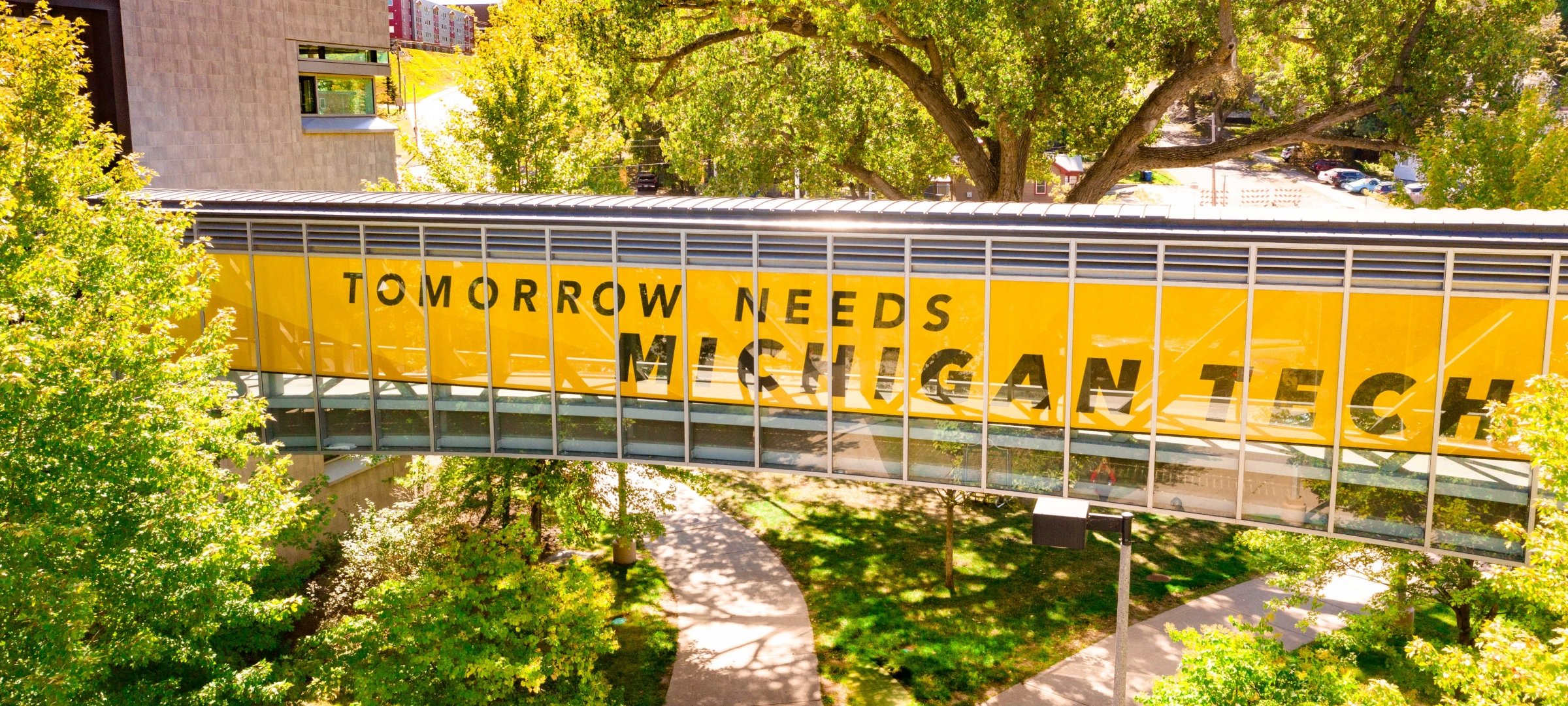 Walkway across campus with "Tomorrow needs Michigan Tech" slogan on the windows of the walkway. 