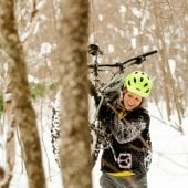 Female biker carrying a bike on the snow covered trails.