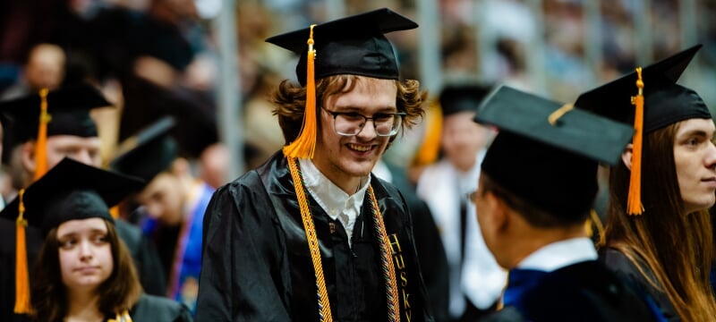 A smiling student in a cap and gown at commencement