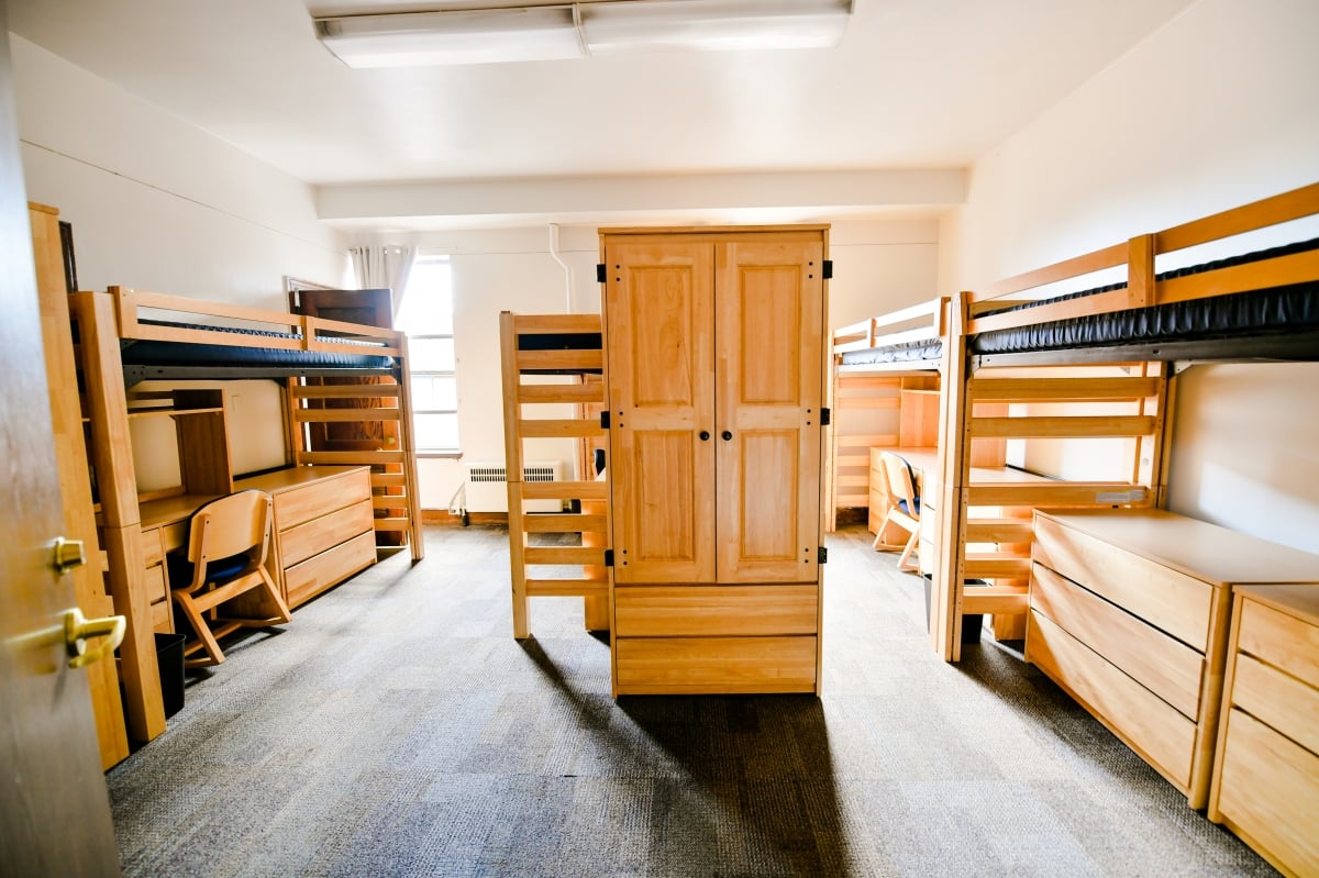 Three loft beds with desks below and a wardrobe in the middle with another bed behind it.