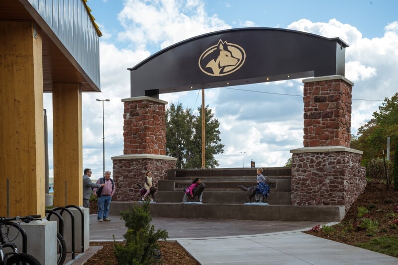 East Patio looking east, East entrance to campus sign with running husky statues.
