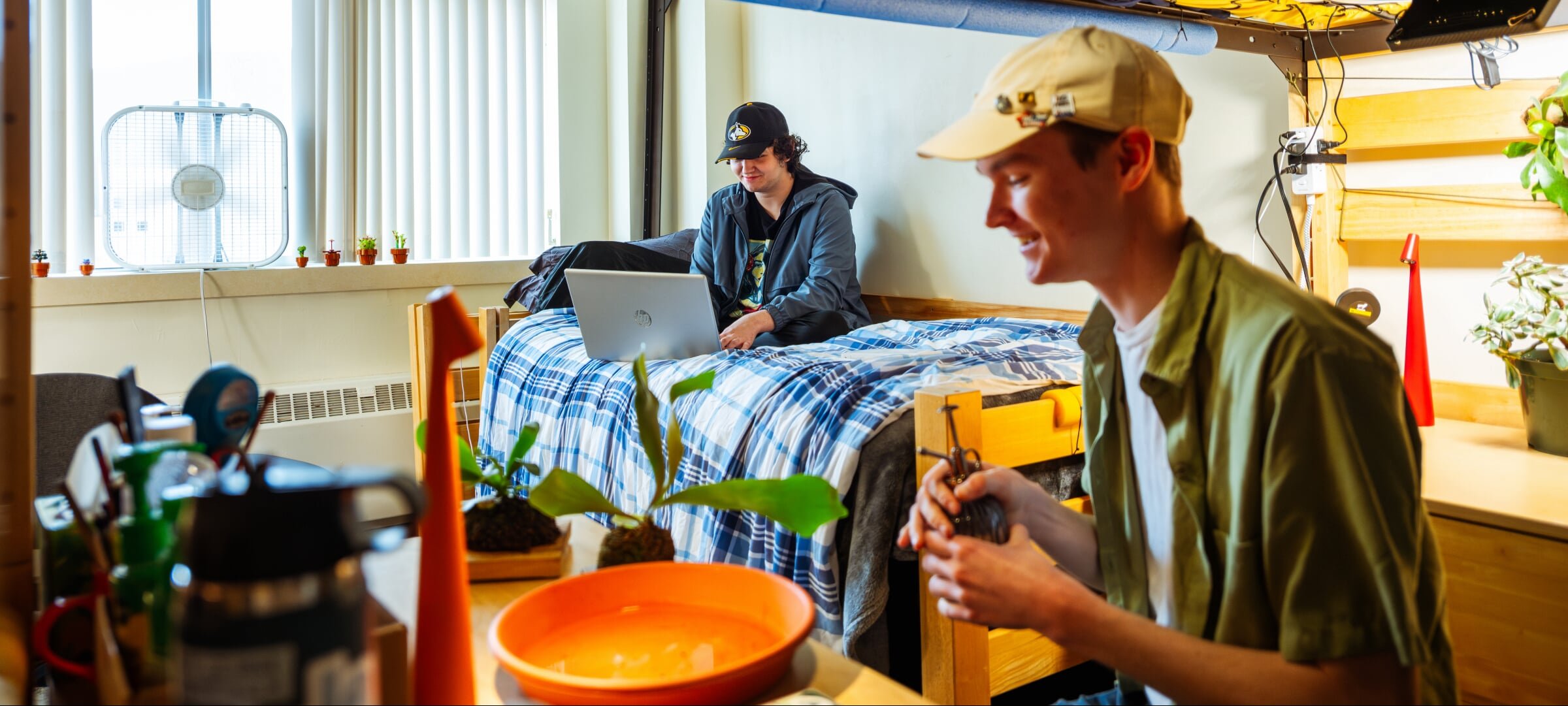 Two students in a dorm room with one sitting on the bed and the other at their desk