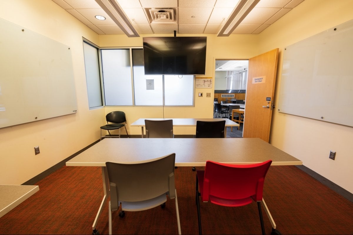 Small meeting room with white boards, two tables tables, a TV, and chairs.