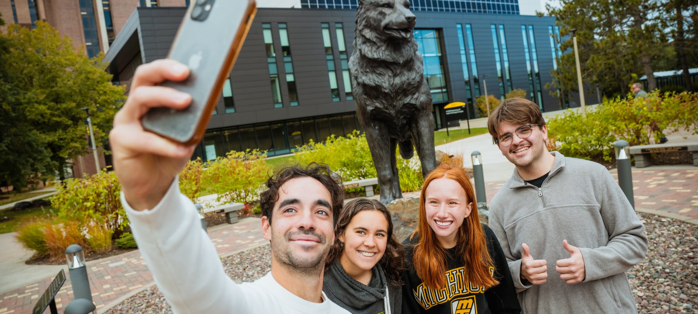 Four students taking a selfie at the Husky Statue on MTU campus.