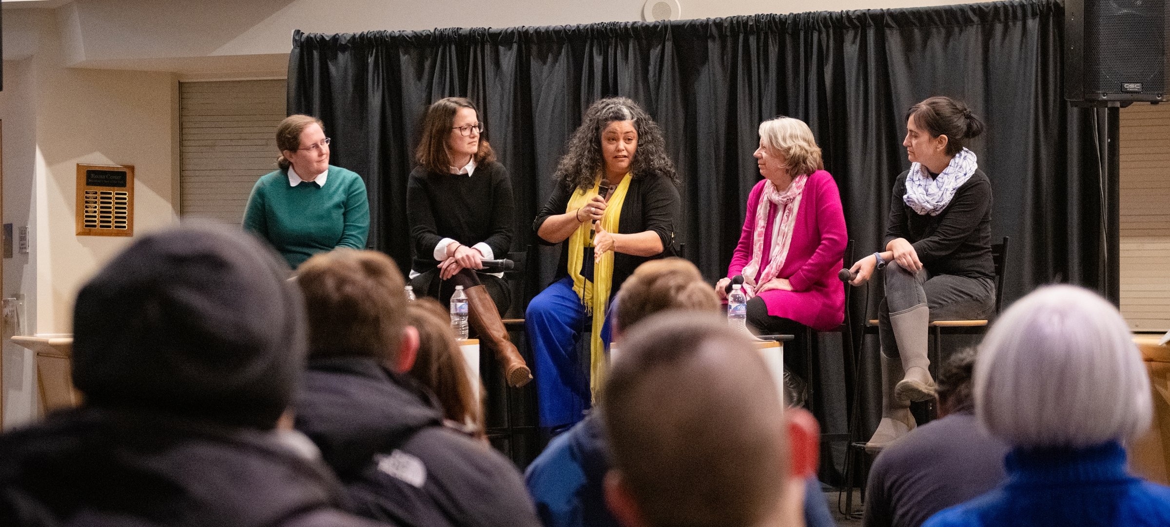 Women in a panel discussion in front of a crowd of people.