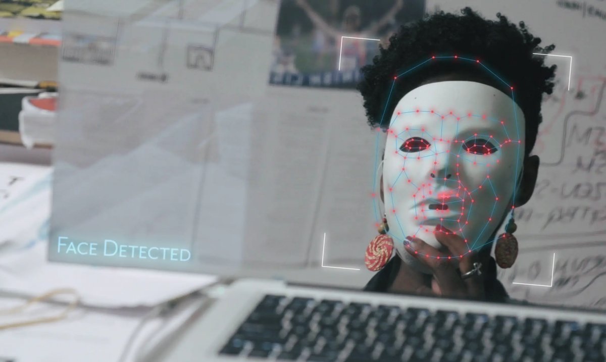 A black woman holding a white mask in front of her face while looking in the mirror