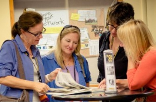 Four female alumni peruse a yearbook.