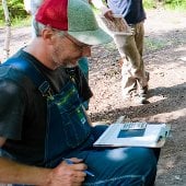 A man in overalls writes information on a clipboard.