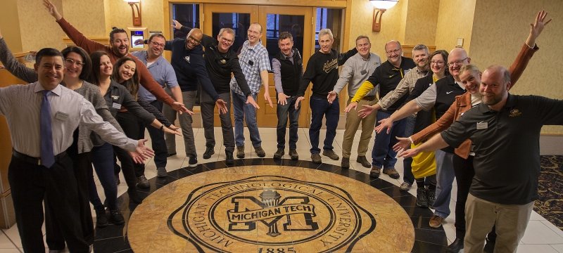 Alumni Board of Directors standing around the MTU seal with arms out