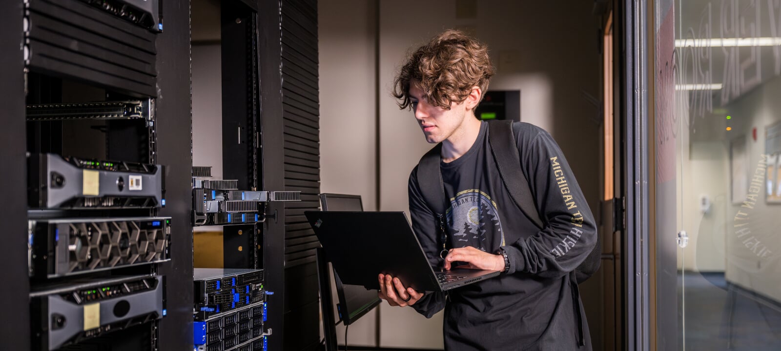 A student operates a laptop computer while managing servers in a server room