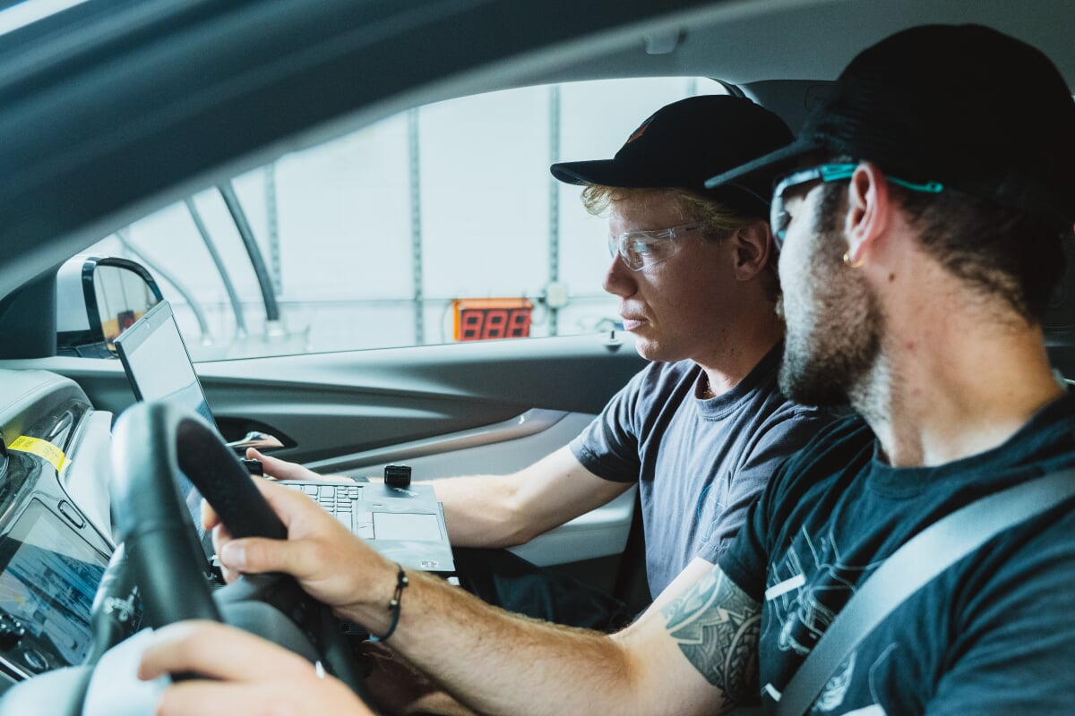 2 people sitting in a parked car looking at a computer.