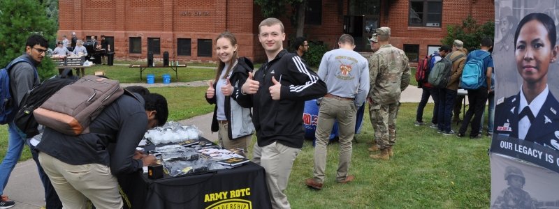 Event outside of the ROTC building, students signing on a table and a couple giving a thumbs up