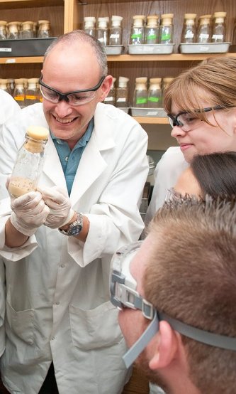 Faculty showing students the contents of a corked bottle with gloves and goggle in a labcoat