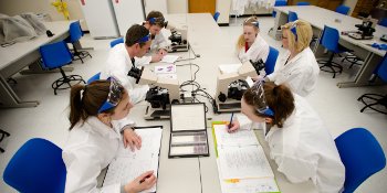 Students sitting at a table working on microscopes.