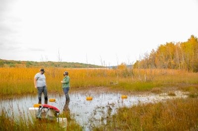 Amy and student in pond with trees in the fall