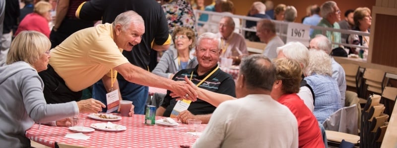 Alumni reaching across a round table to shake hands with another.