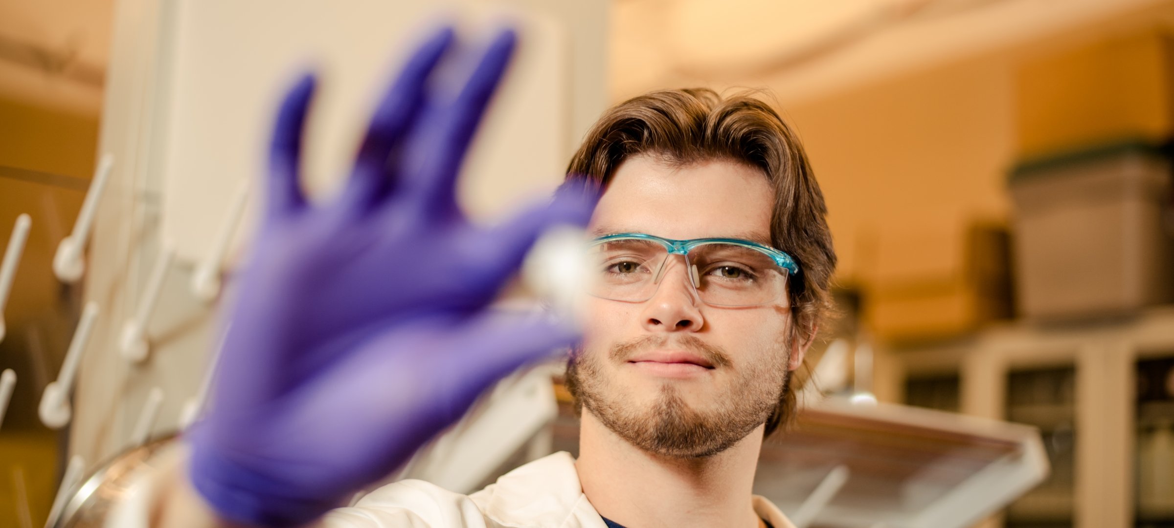 Researcher, wearing a lab coat and gloves, holding a sample