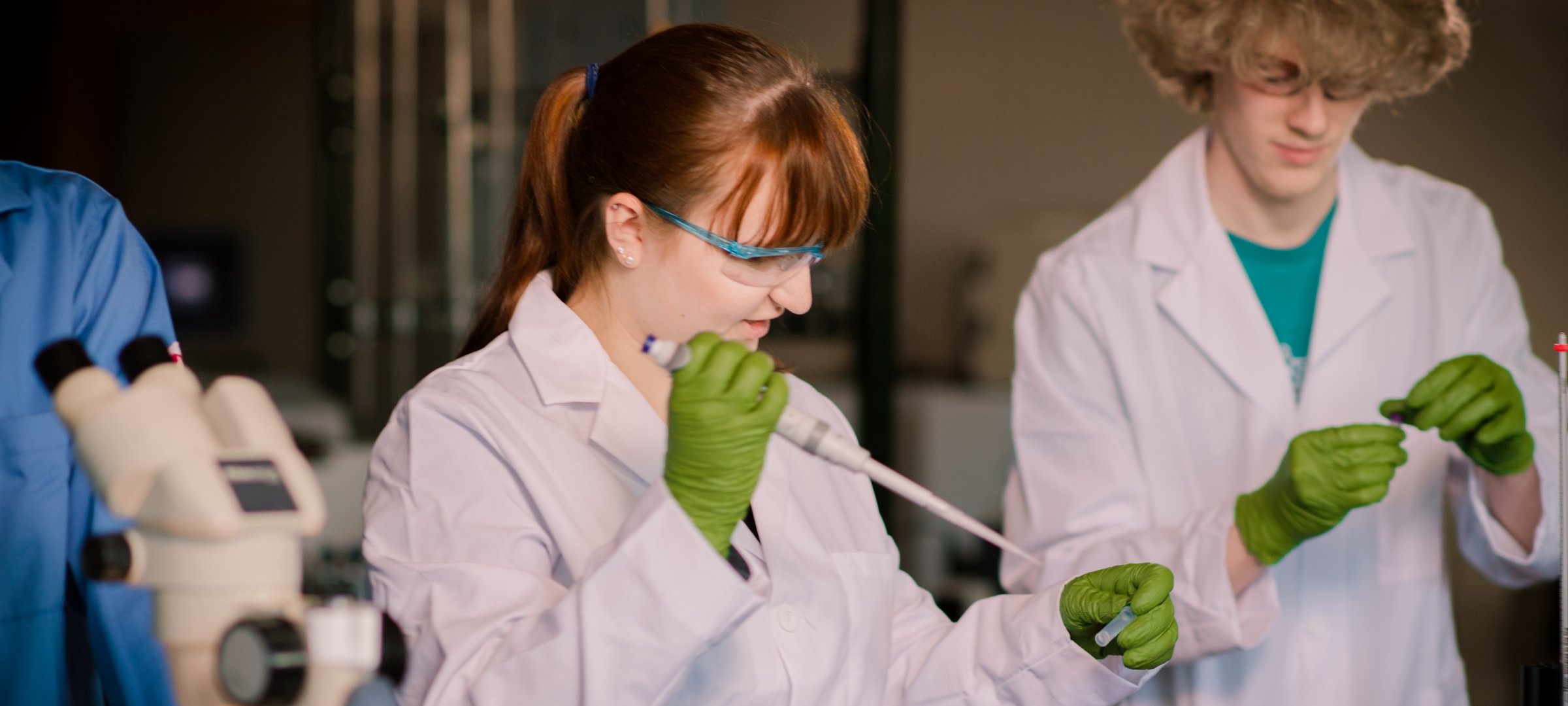 Three students, wearing lab coats, working in a bioinformatics laboratory