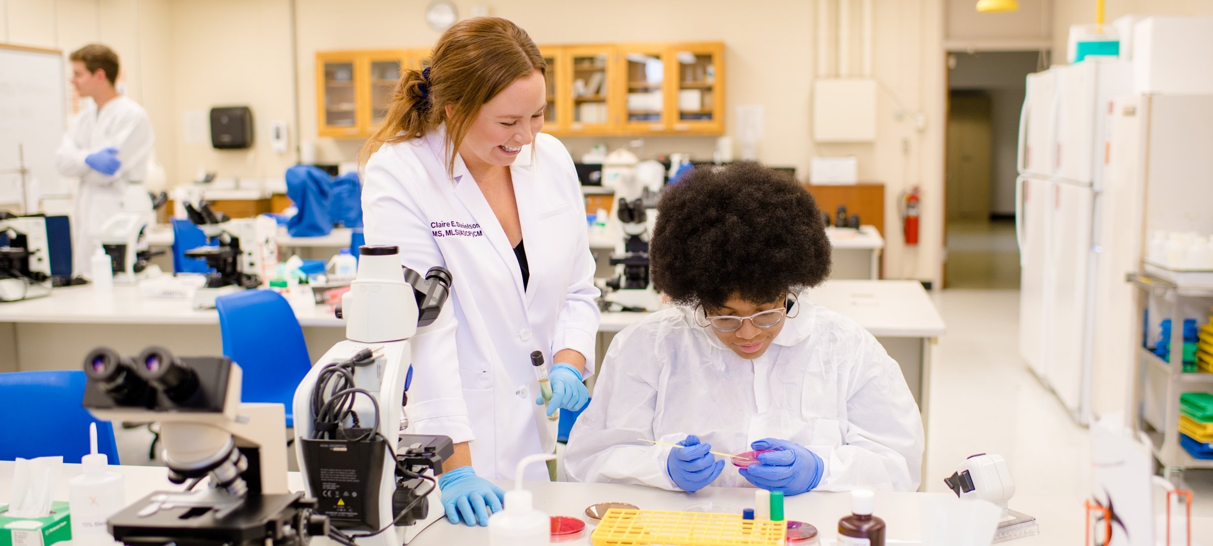 Student and instructor, wearing lab coats, performing microbiology lab tests