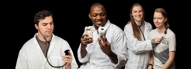 Four students in lab coats two are holding a stethoscope and one is holding a model of a tooth.