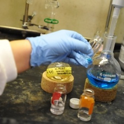 Gloved hand holding a vial with other beakers and vials on a table.