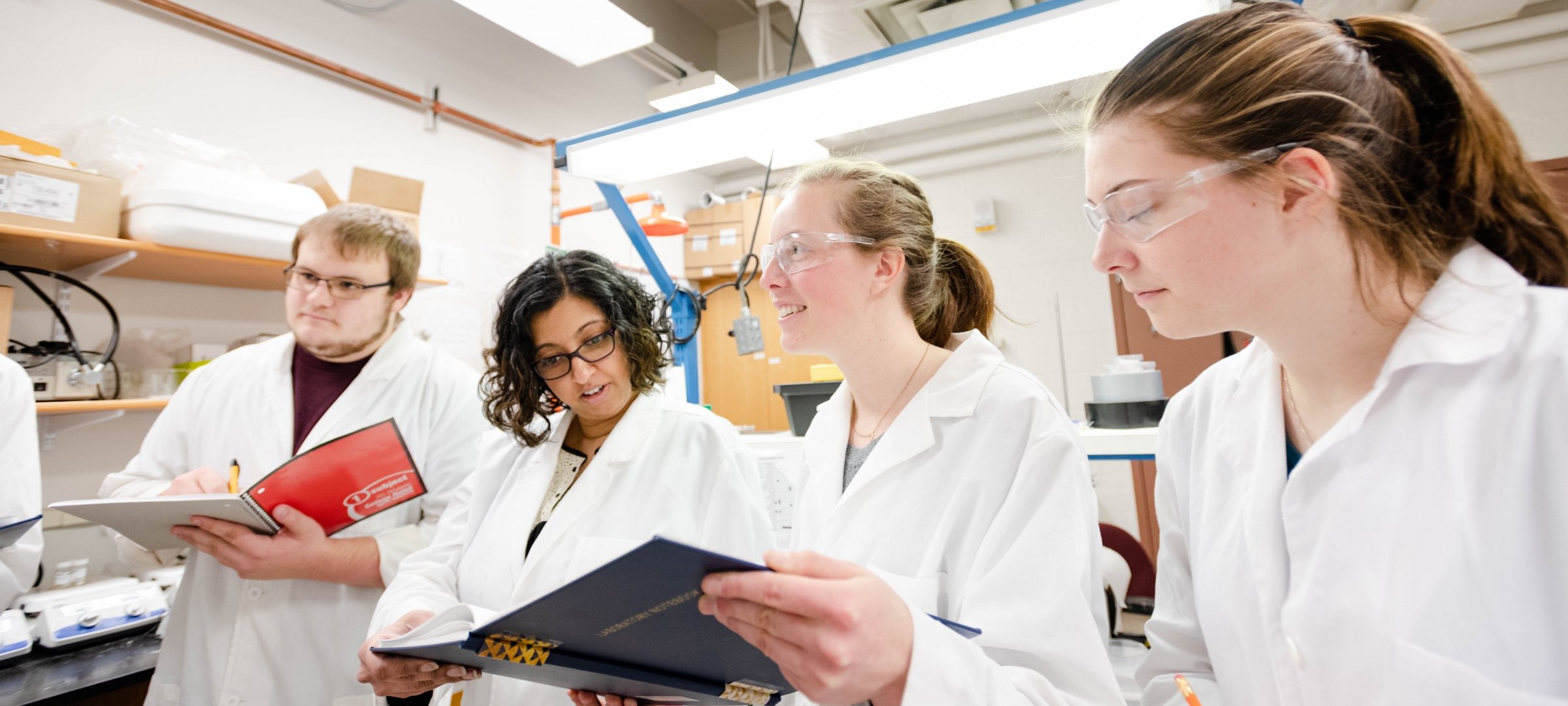 Professor and three students reviewing notes in a lab.