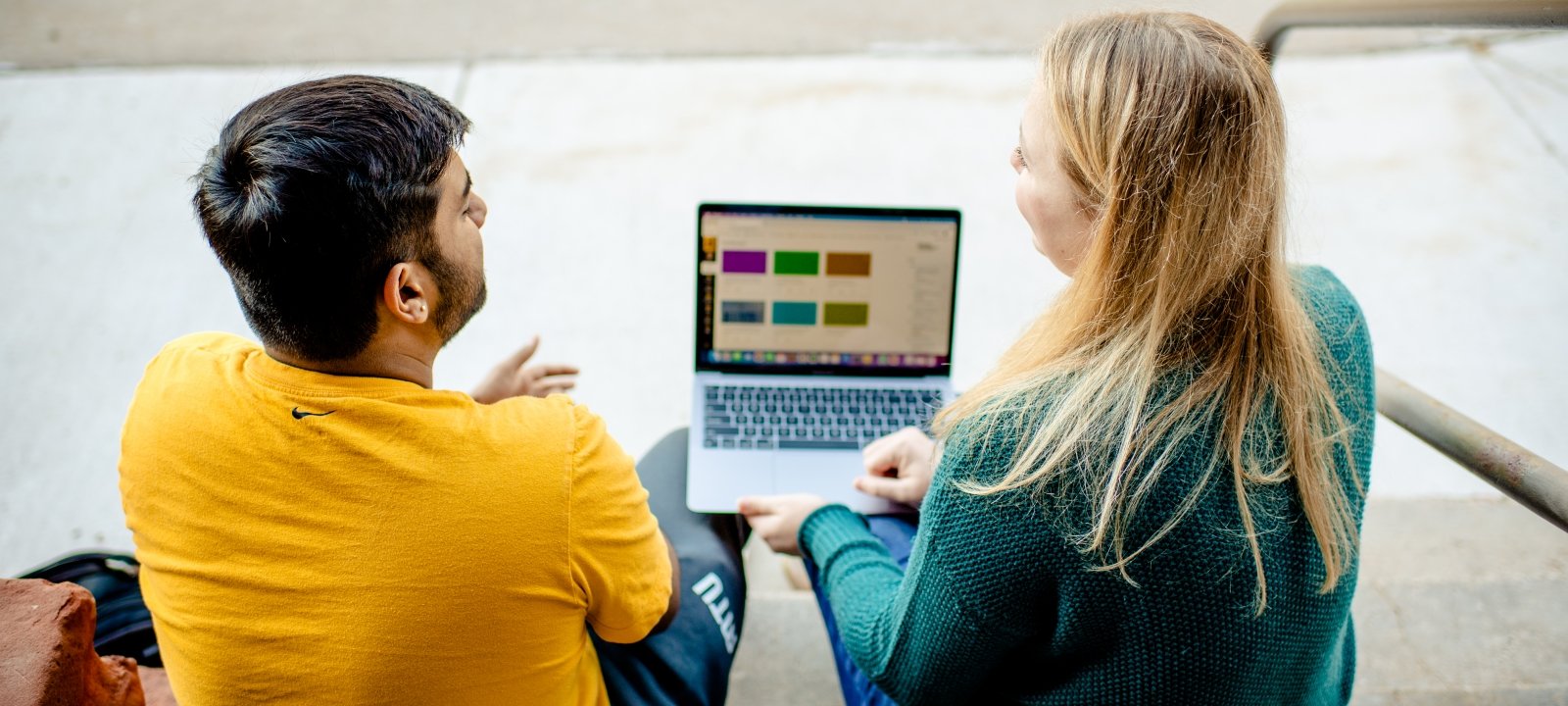 Two students looking at charts on a laptop discussing business analytics