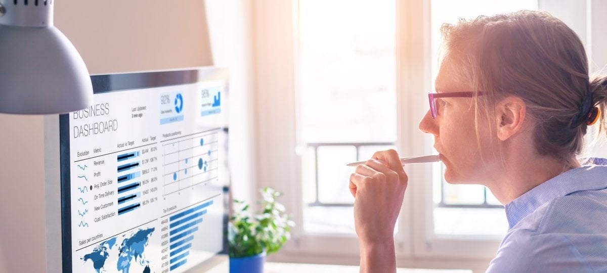 Image of businesswoman chewing on a pencil looking at a computer monitor showing a business analytics dashboard