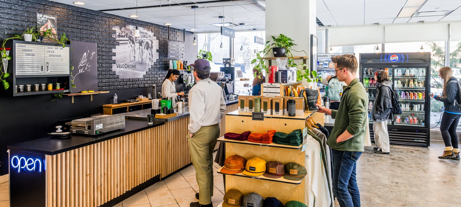 Students stand around Velodrome, a cafe counter with a drink cooler and merch stand.