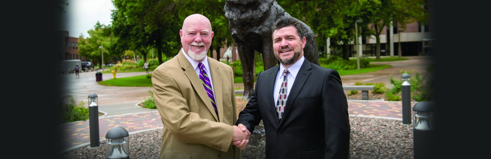 Gene Klippel and Dean Johnson shaking hands in front of the Husky statue