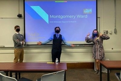 Three AMA students in front of a presentation on a screen.