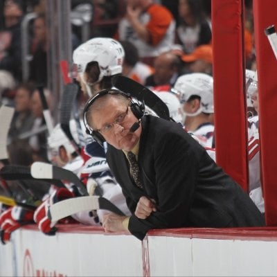 Steve Coates leaning over the ice ffrom the players bench.