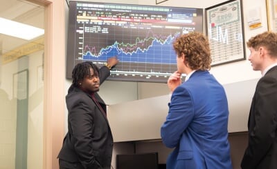 Elijah Joseph pointing to a line chart on a TV screen while other students look on.