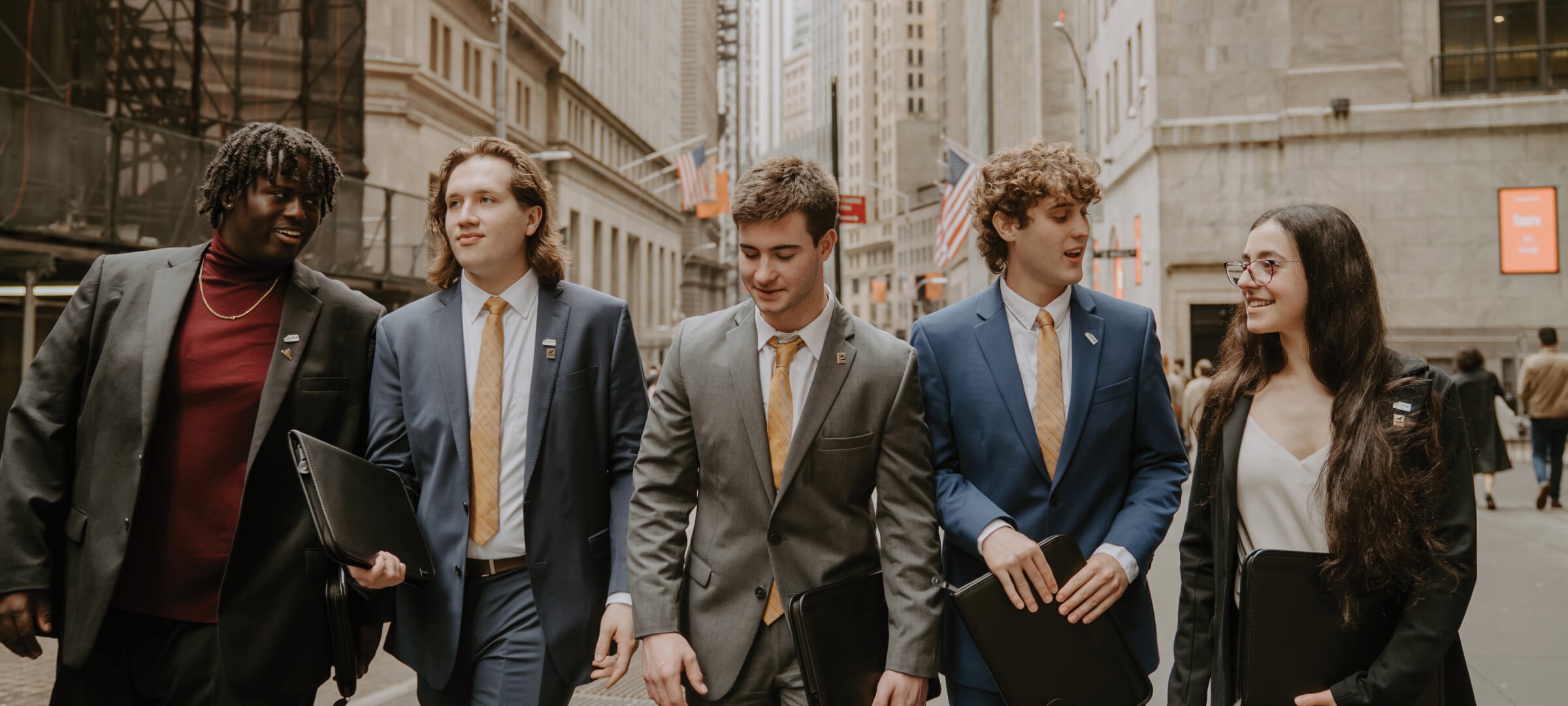 Five students in suits walking down a city street.
