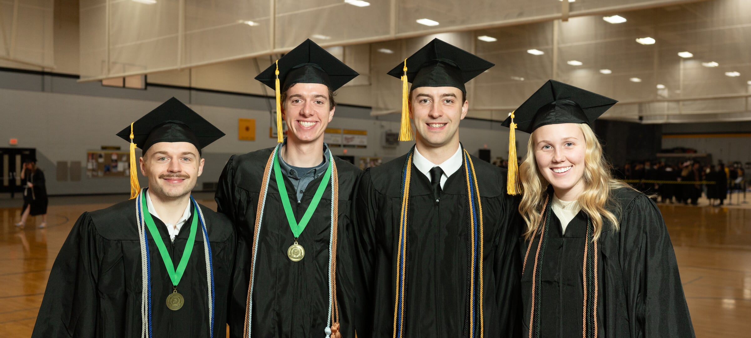 Four students in caps and gowns pose together.