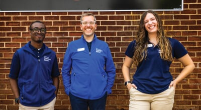 Three people in Michigan SBDC shirts standing in front of a brick building.